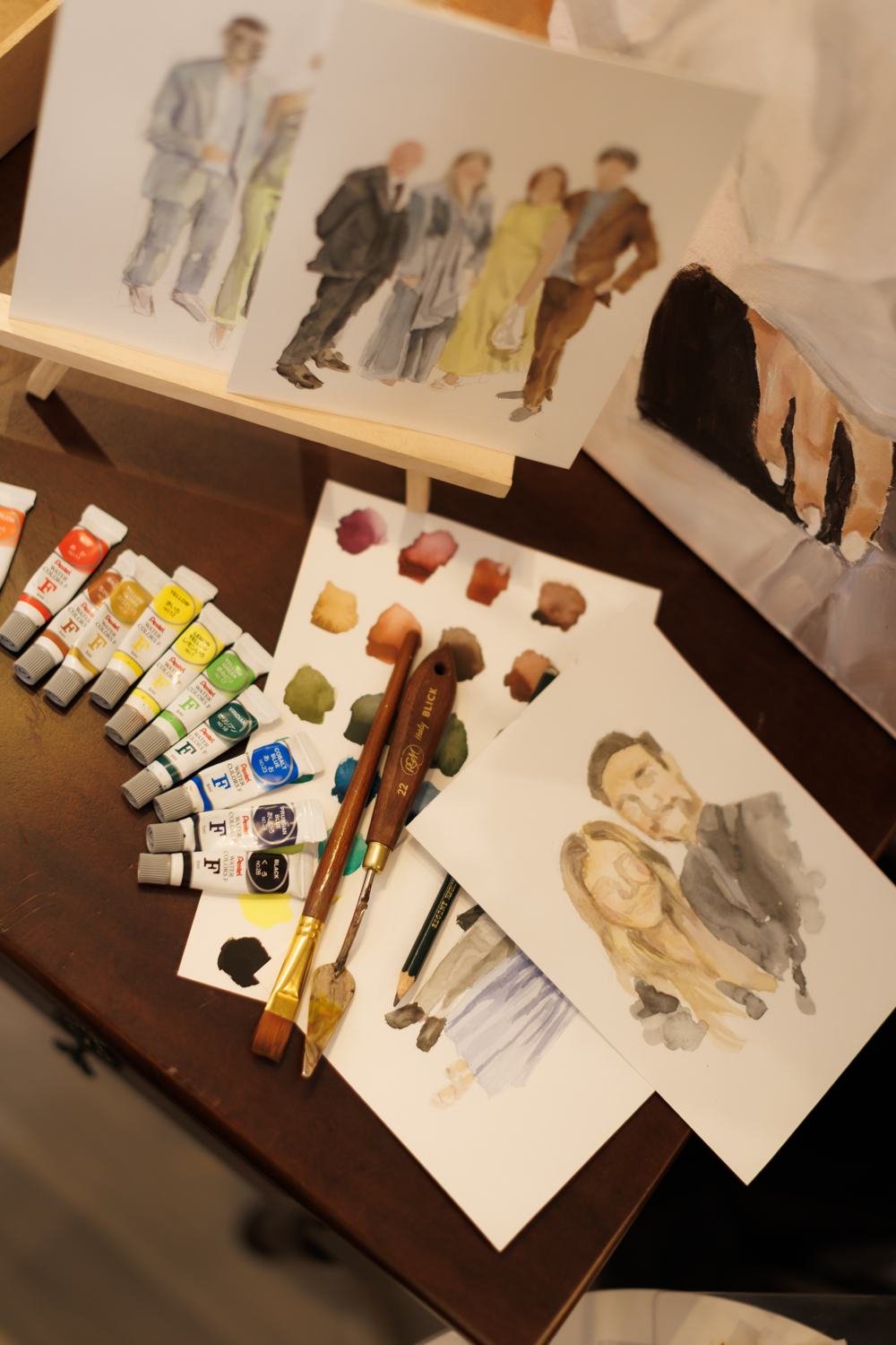 Mesa com tubos de aquarela e retratos prontos